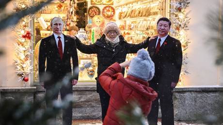 A man poses for a photo with cardboard figures of Russian President Vladimir Putin and Chinese President Xi Jinping in Moscow.
